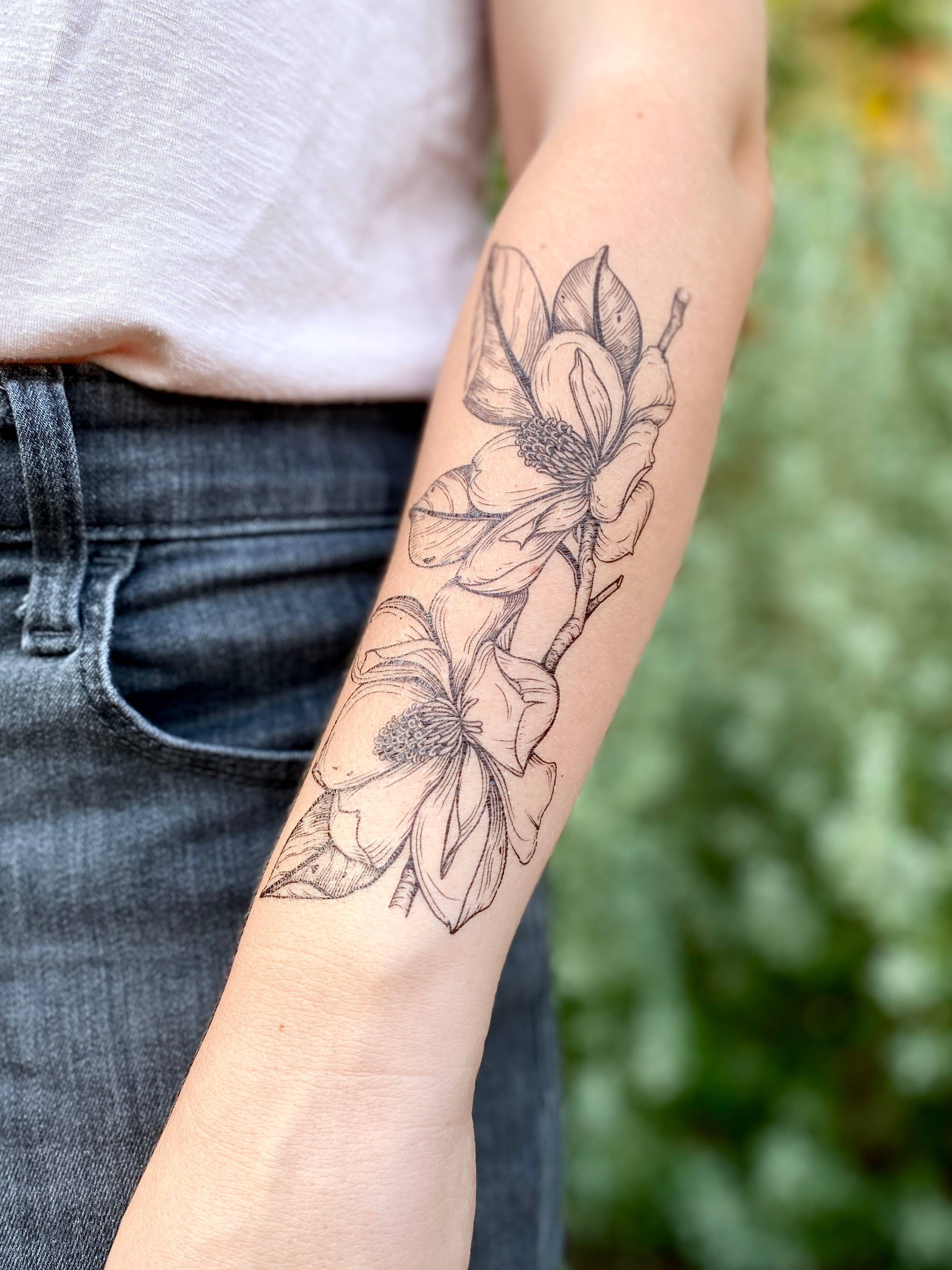 Magnolia Flowers temporary tattoo 2 pack! This hand-drawn floral design measures 6.25 by 2.5 inches with black lines and stippling.

This pair of southern magnolia flowers are attached to a thin branch with four fresh leaves surrounding the petals.

All t